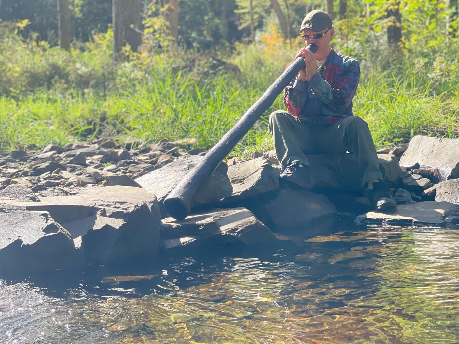 Playing the didgeridoo on the rocks beside a forest creek
