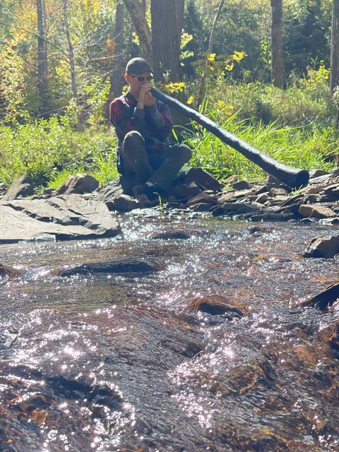 Playing the didgeridoo by a sparkling forest creek