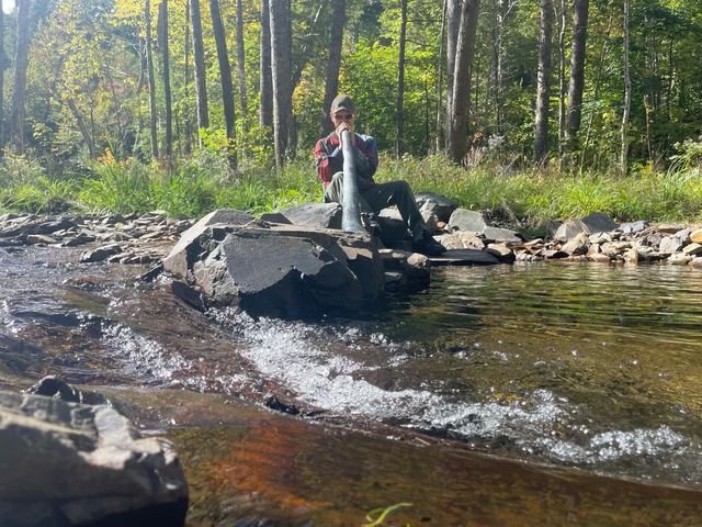 Playing the didgeridoo beside a flowing creek