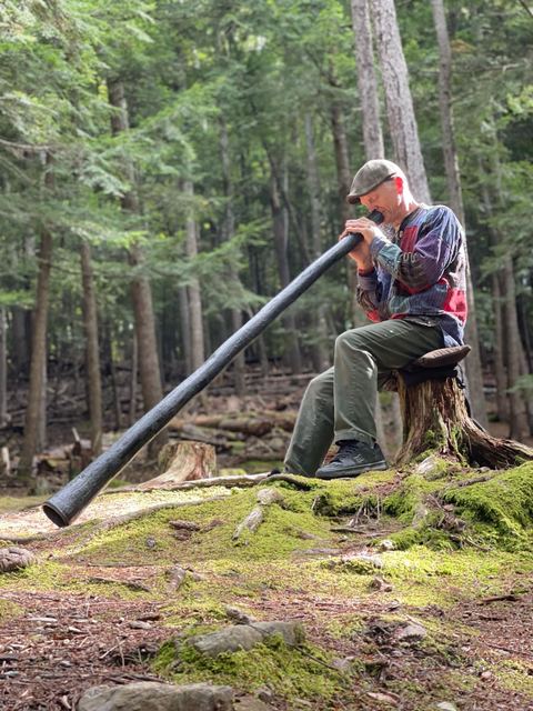 Playing the didgeridoo on a mossy stump in the forest