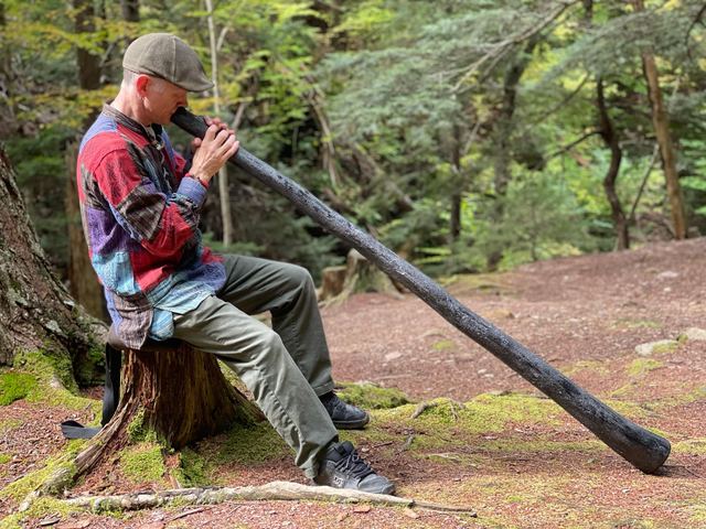 Side view of playing a long dark didgeridoo in the forest