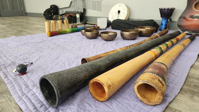 Four didgeridoos laid out beside singing bowls