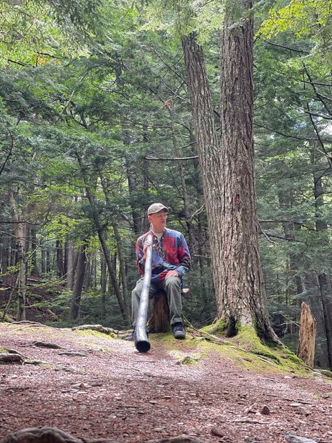 Resting with a didgeridoo beside a large forest tree